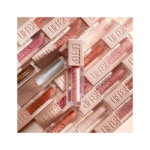 Plusieurs tubes de « Lifter Gloss Brillant À Lèvres » de Maybelline New York, de différentes teintes, sont disposés à l'horizontale, tandis qu'un tube est placé à la verticale au centre. Dakar