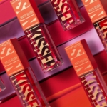 Plusieurs flacons de « Sunkisser Matte Blush Liquide Effet Mat » de Maybelline New York sont disposés en diagonale sur un fond rose vif et orange, chacun arborant un texte graphique et audacieux sur son emballage. Dakar