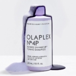 Une bouteille de shampooing tonifiant Olaplex No. 4P Blonde Enhancer avec du shampooing violet moussant par le haut et s'accumulant autour de la base. L'étiquette indique les avantages du produit et le format de 250 ml. Dakar