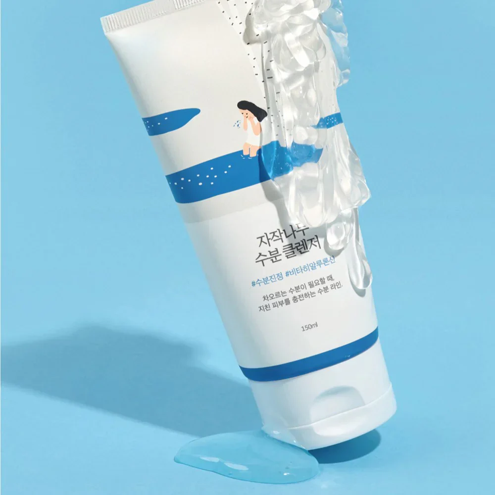Un tube de « Round Lab Nettoyant Hydratant à l’Acide Hyaluronique et Sève de Bouleau » de 150 ml, dans un emballage bleu et blanc orné d’une illustration représentant une fillette, repose sur un fond bleu, tandis qu’un gel transparent s’écoule de son embout. Dakar