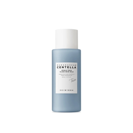 Un flacon cylindrique bleu muni d'un bouchon blanc, portant l'étiquette « Skin1004 Hyalu Teca Glass Skin Milk Essence Lactée Hydratante et Éclat 210 ml », est posé à la verticale sur un fond blanc. Dakar
