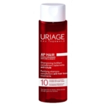 Un flacon rouge de shampooing fortifiant pour les cheveux d'Uriage AP pour les traitements anti-chute, étiqueté pour la chute et la croissance des cheveux, avec un bouchon blanc et un texte blanc et rouge détaillant ses avantages. Dakar