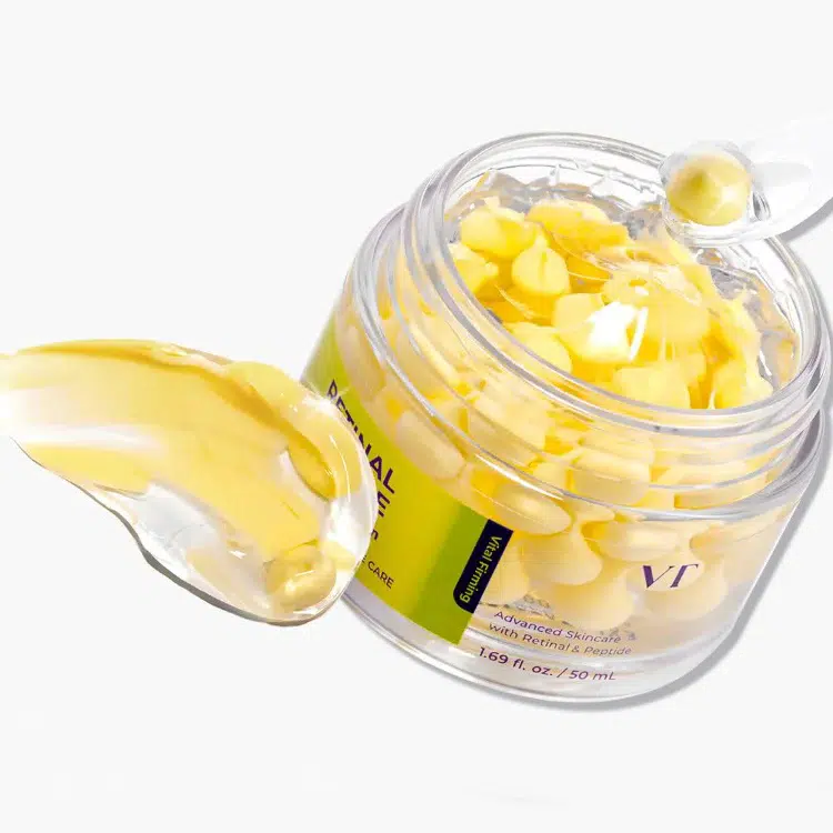 Un pot ouvert de « Vt Crème en Capsules aux Peptides Rétiniens Anti-Rides et Ridules » de 50 ml, avec une cuillère transparente servant à prélever une capsule jaune, et une touche de crème jaune à côté du pot sur un fond blanc. Dakar