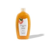 Un flacon en plastique transparent contenant le gel douche exfoliant « Routine Glow Sunshine Éclat du Teint » de Byphasse, à l'huile d'argan. Le gel de couleur orange contient de petites billes, et l'étiquette blanche comporte un texte ainsi qu'une illustration représentant un fruit d'argan. Le flacon projette une ombre sur le fond blanc. Dakar