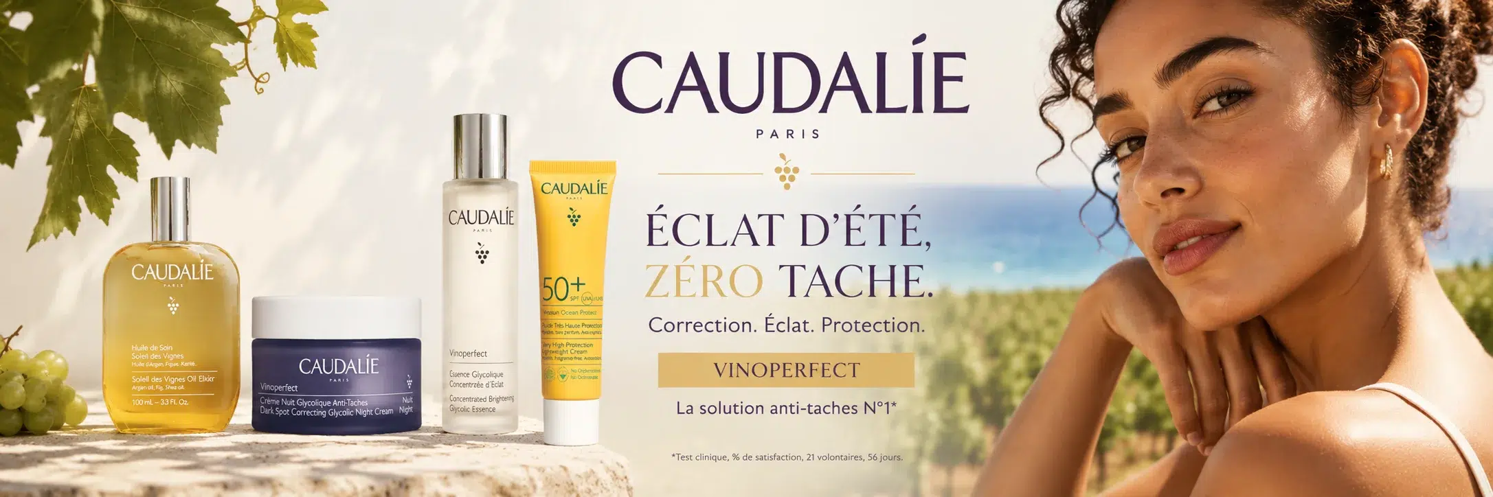 Les produits de soin Caudalie sont présentés en extérieur, avec des grappes de raisin, un mur de pierre et la mer en arrière-plan. Une femme aux cheveux bouclés regarde l'objectif pour promouvoir la gamme anti-taches Vinoperfect de Caudalie, disponible chez Univers Cosmetix pour tous vos produits de beauté indispensables. Dakar