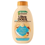 Un flacon beige de shampoing Garnier Ultra Doux à l'huile d'argan et à la crème d'amande, destiné aux cheveux secs à très secs. Le design met en avant des noix d'argan et des touches de bleu. Dakar