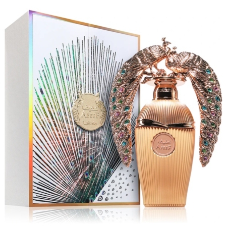 Un luxueux flacon de parfum doré, orné de deux paons sculptés et sertis de pierres précieuses se faisant face, posé à côté d'un élégant coffret irisé, décoré d'un motif en forme d'éventail et arborant un emblème doré portant l'inscription « Attar Al Firdaws ». Dakar