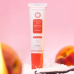 Un tube de gel parfumant Musc Intime « Hot Peach La charmeuse » de 30 ml est posé à la verticale sur une surface blanche, entouré de moitiés de pêche et d’une gousse de vanille, le tout sur un fond rose pâle — une scène aussi séduisante que La charmeuse elle-même. Dakar