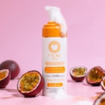 Un flacon de mousse nettoyante « Musc Intime », surmonté d'une couche de mousse, est entouré de fruits de la passion entiers et coupés en deux, sur un fond rose. Dakar