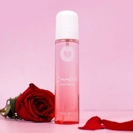Un flacon rose de « MUSC Rose Mystik l'Envoutante Brume corps » de 120 ml est posé à la verticale à côté d'une rose rouge et de pétales de rose éparpillés sur une surface rose, le tout sur fond rose. Dakar